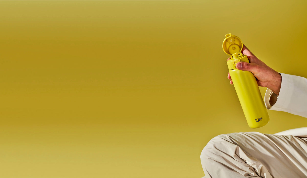  A yellow ION8 water bottle is held open against a yellow background by a person wearing beige clothing.