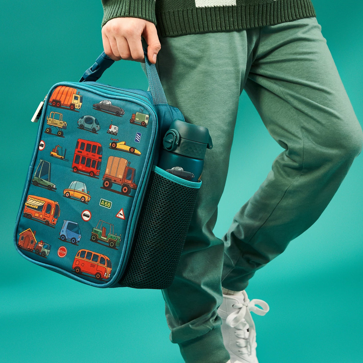A rectangular teal lunchbox showcases colorful cartoon vehicles including cars, buses, and trucks with road signs such as "Stop" and "A68" in a playful pattern.