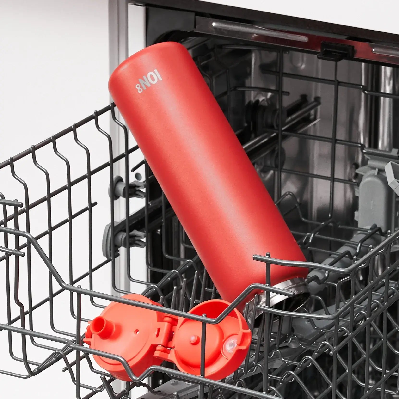 A red ION8 water bottle is being washed inside a dishwasher's wire rack.